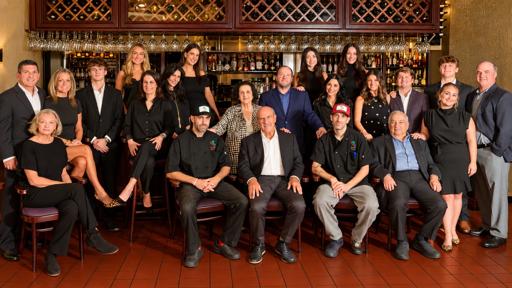 The Marino family gathered in Gino's dining room, chefs seated in front with family standing behind them before the wine cabinets