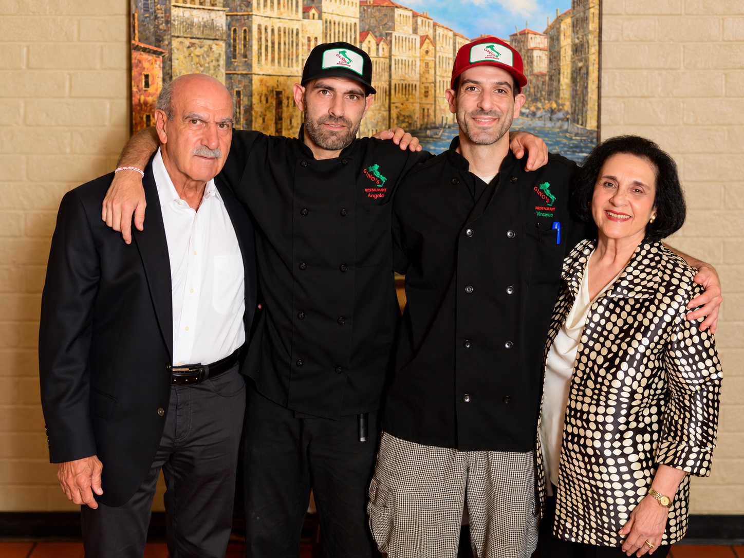 Chefs Angelo and Vincenzo in their Gino's chef coats, arms around their parents in front of a Venice mural